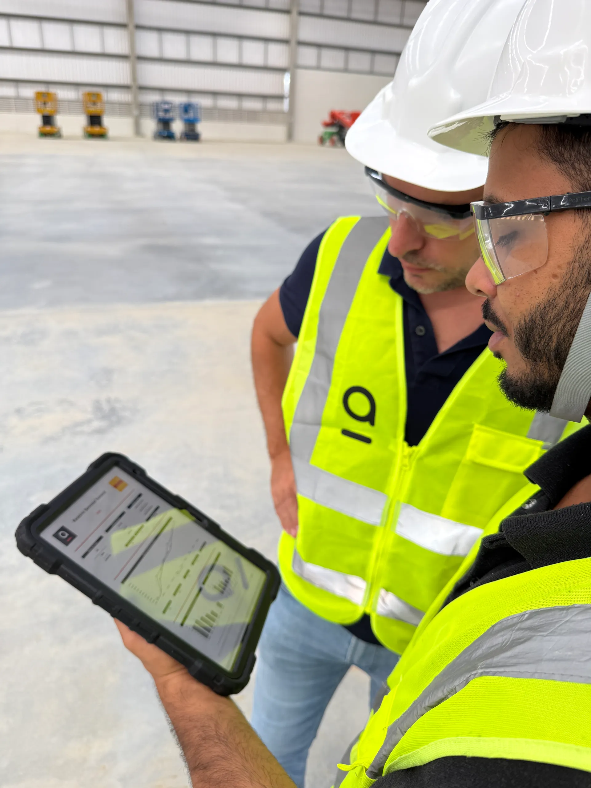 Dois profissionais da Agio, de capacete e colete, analisando o relatório do projeto em tablet no canteiro